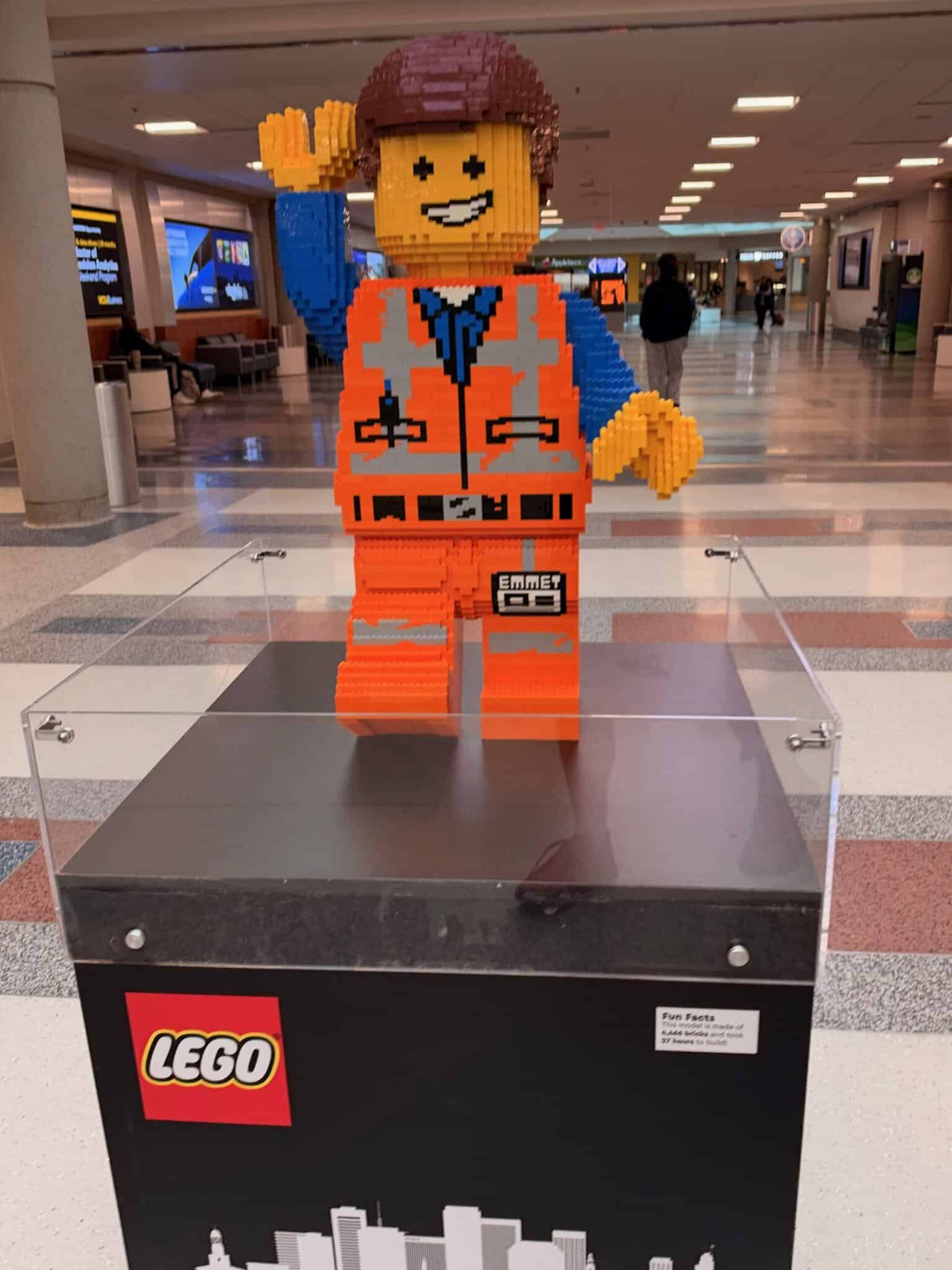 Life-size LEGO figure in an orange construction vest waving from a display case in the RIC airport concourse