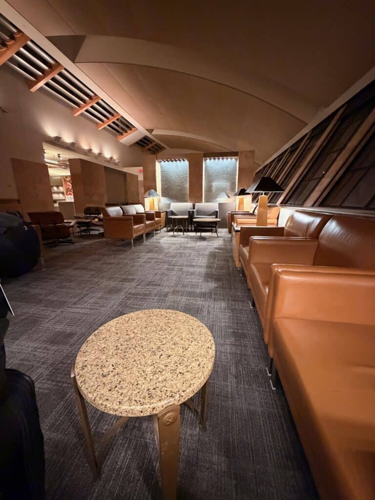 The interior of an American Airlines Admirals Club at DFW with leather lounge chairs, warm wood paneling, and tall angled windows - aviation photography by Anthony Yandow