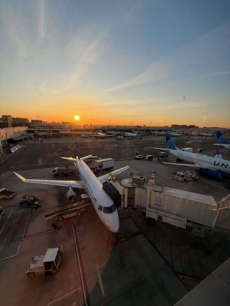 A United Express regional jet at Gate 70A at LAX with the sun rising over the Los Angeles skyline in the background - aviation photography by Anthony Yandow