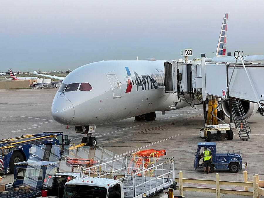 A Boeing 787 at the boarding gate with ground crew doing pre-flight preparations