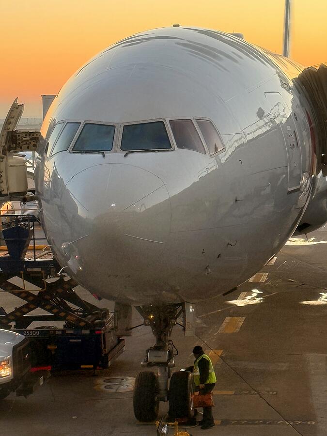 Ground Crew and Boeing 777 at DFW Sunrise A Boeing 777 at the gate at DFW at sunrise with a ground crew member in a safety vest at the nose gear